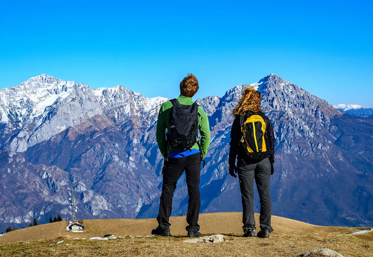 Two hikers with backpacks triumphantly pose atop a majestic mountain peak.
