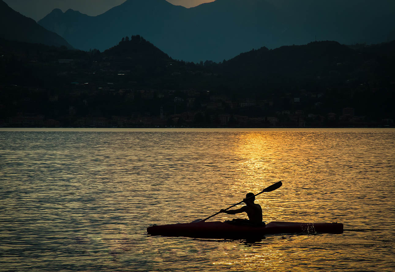 Un kayaker solitario scivola tranquillo su un lago sereno, illuminato dalle calde tonalità di un tramonto mozzafiato.