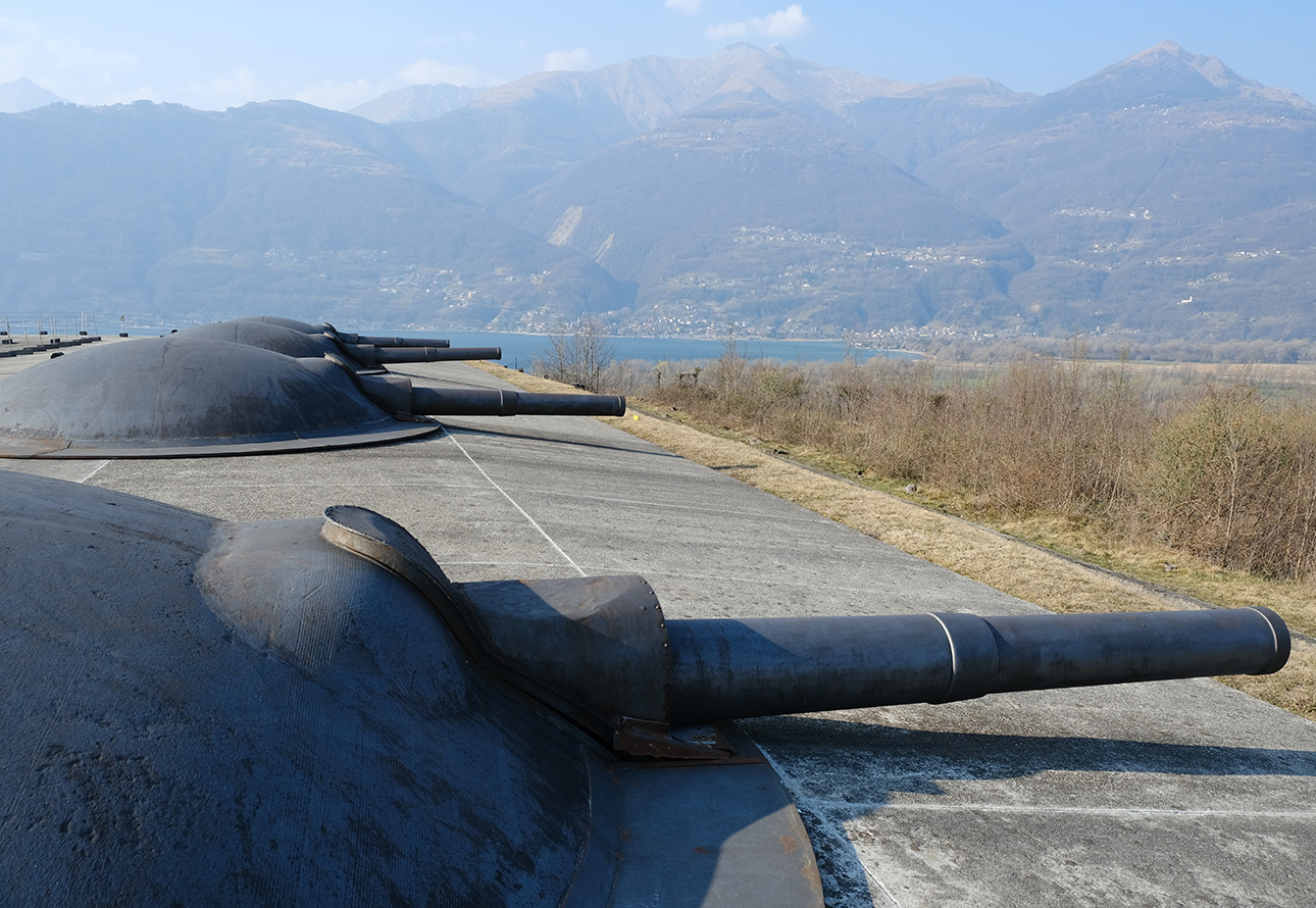 A concrete wall adorned with a substantial array of cannons with the lake and mountains view in the backgroud