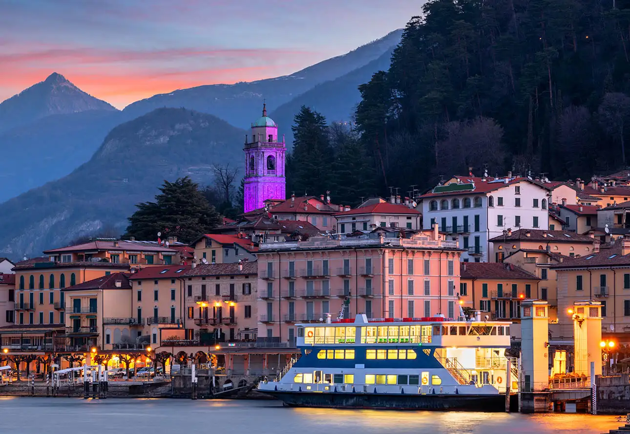 A river boat is docked in front of a town, showcasing the Bellagio Waterfront evening lights and offering a colorful view