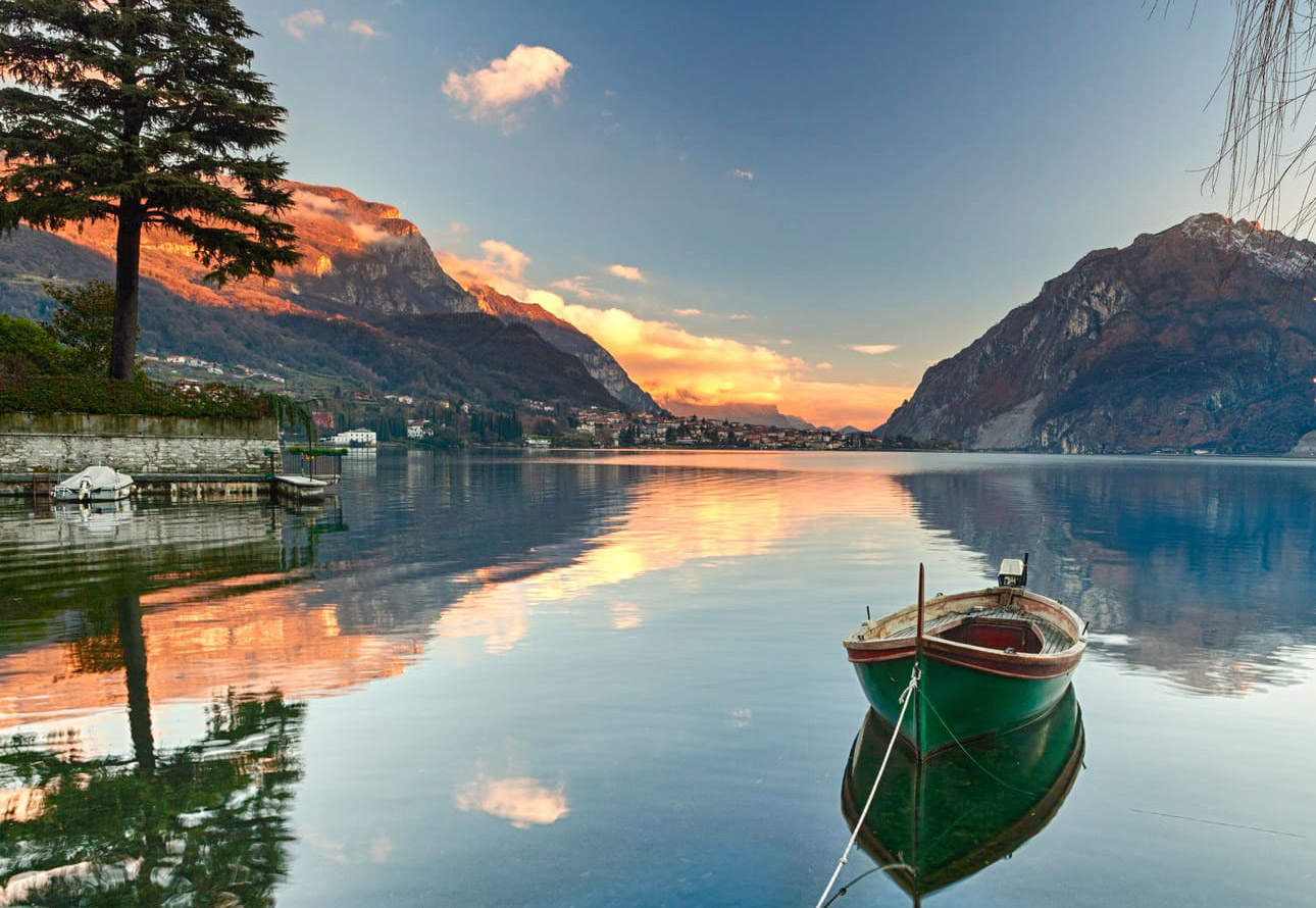 A boat is anchored on the serene lake, with towering mountains as its backdrop.