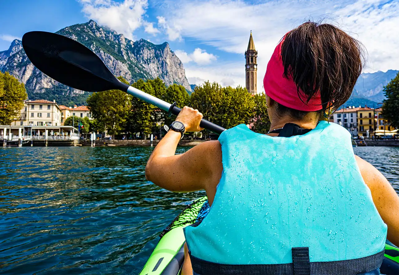 A female kayaker gracefully propels her paddle through calm waters on a serene lake.