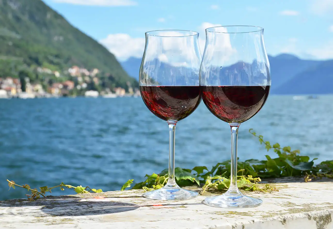 two wine glasses brimming with red wine, set against the backdrop of a tranquil lake