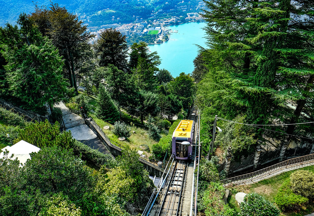 Un teleférico que asciende una montaña, rodeado de frondosos árboles y un sereno lago de Como.
