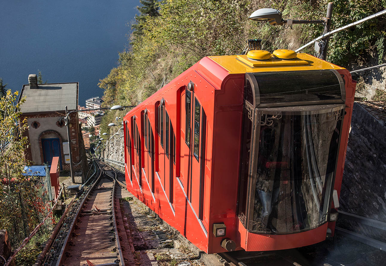 Czerwono-żółty pociąg na torze przedstawiający kolejkę linową Como – Brunate