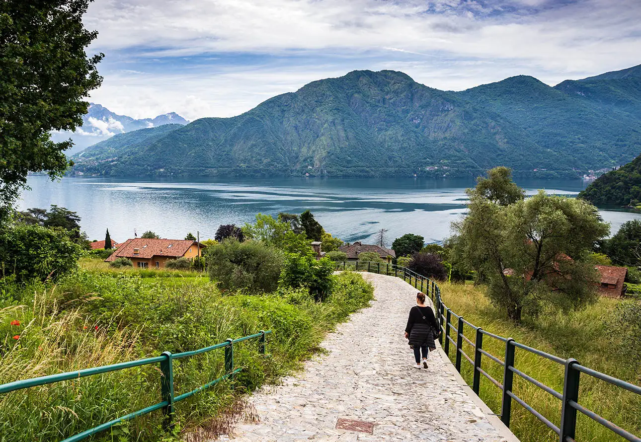 A person strolling along a path adjacent to a serene lake enjoying Greenway of Lake Como looking at the picturesque lake and mountain view