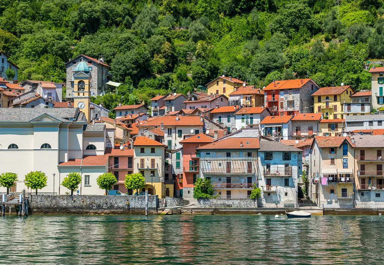 A town on the shore of a lake with many colorful buildings, located in Colonno