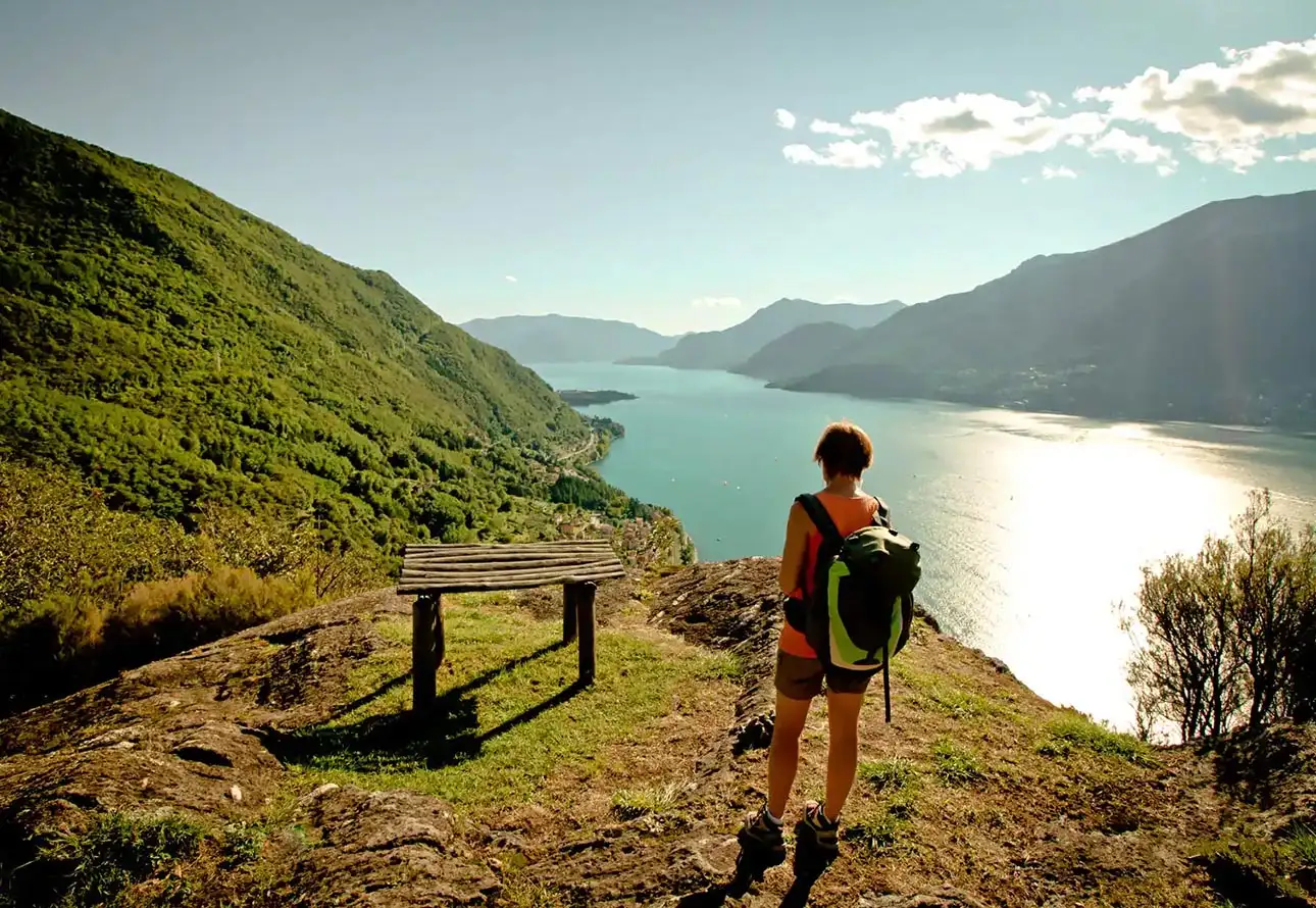 A person with a backpack stands on a Sentiero del Viandante, a renowned hiking trail gazing at a breathtaking view of Lake Como