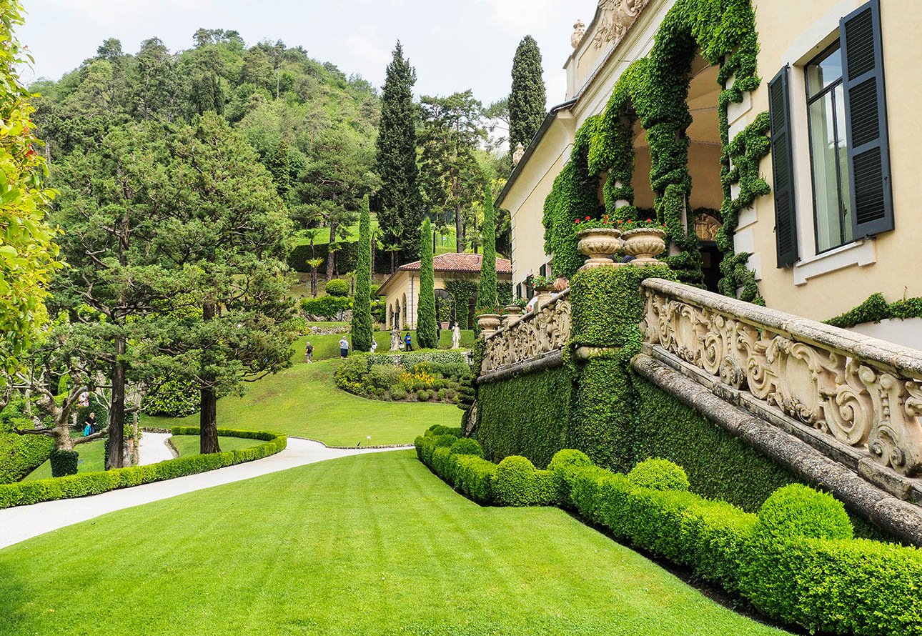 Auf dem Bild ist ein prächtiges Haus mit einer riesigen Rasenfläche und einem hoch aufragenden Baum zu sehen, umgeben von den atemberaubenden Gärten der Villa del Balbianello