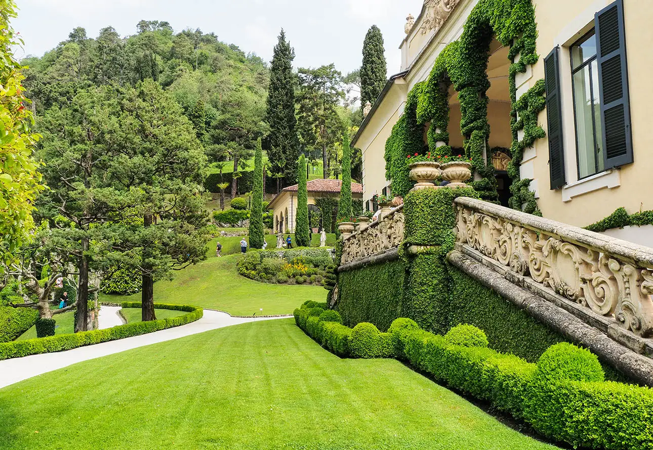 A magnificent house with a vast lawn and a towering tree is captured in the image, surrounded by the stunning gardens of Villa del Balbianello